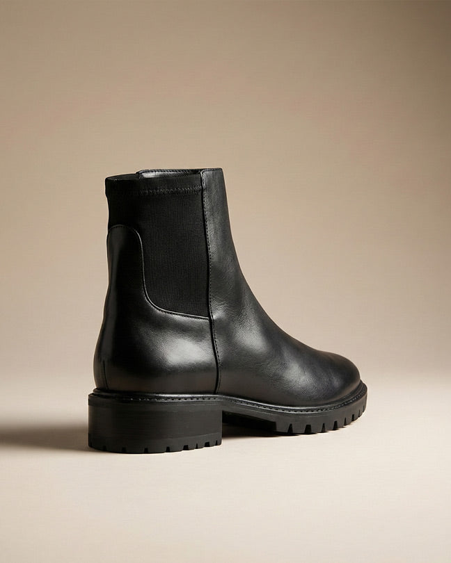 Black leather ankle boot with chunky sole and elastic side panel on neutral background
