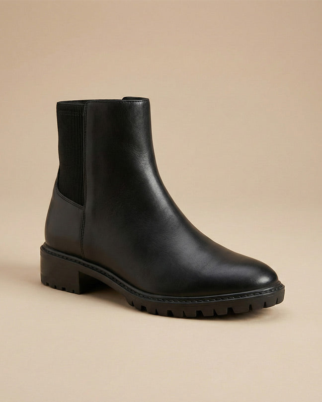 Black leather ankle boot with chunky sole on neutral background