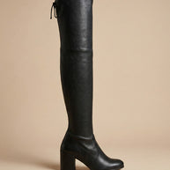 Black over-the-knee high heel boot with block heel and tie detail on beige background