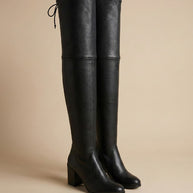 Black over-the-knee block heel boots with tie detail on neutral background