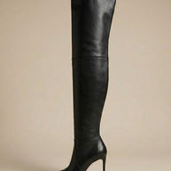 Black over-the-knee leather stiletto boot with pointed toe on neutral background