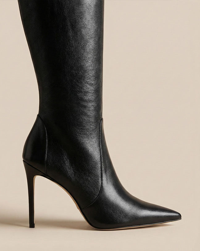 Black knee-high leather stiletto boot with pointed toe on beige background
