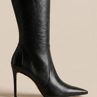 Black knee-high leather stiletto boot with pointed toe on beige background