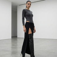 Woman in modern minimalist room wearing black high-slit skirt, grey top, black boots