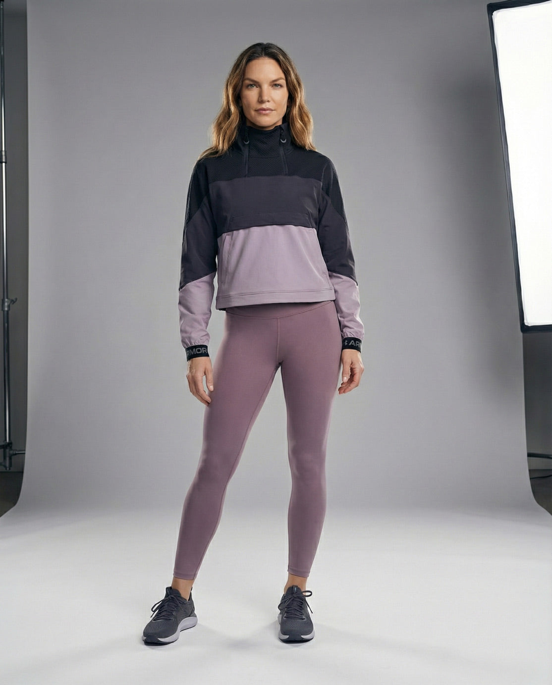 Woman in black and grey athletic pullover and mauve leggings, studio background, sportwear fashion