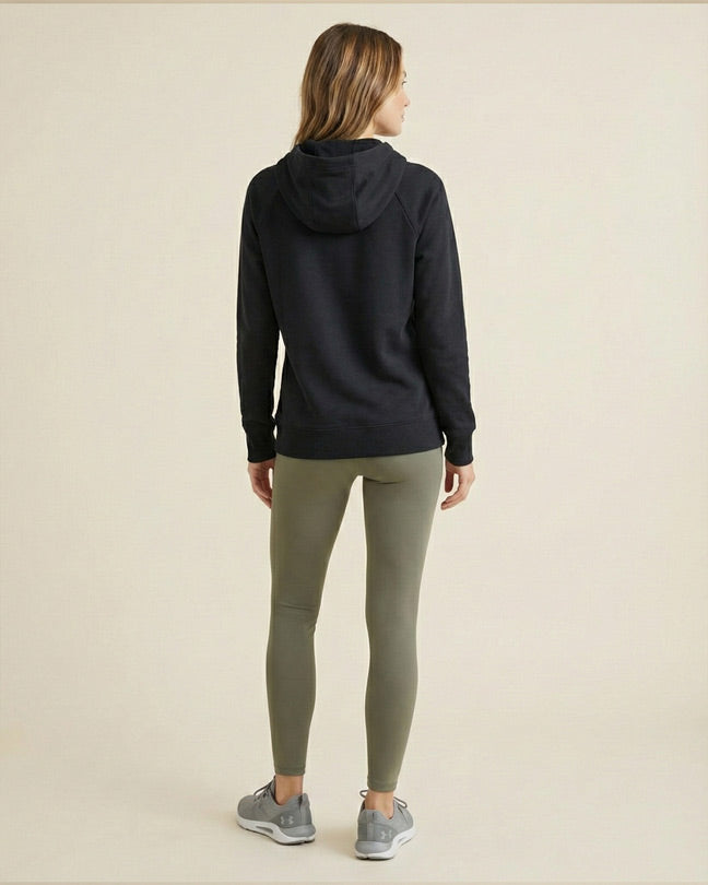 Woman in black hoodie and olive leggings with gray sneakers facing away in studio