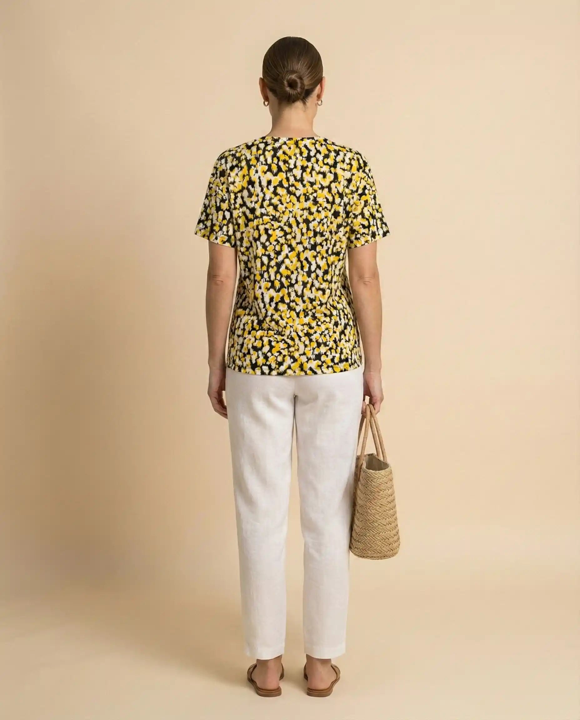 Woman in a yellow and black dotted t-shirt, white pants, holding a straw tote bag