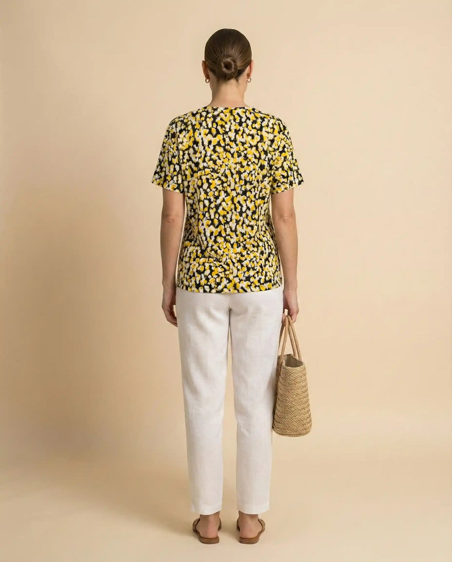 Woman in a yellow and black dotted t-shirt, white pants, holding a straw tote bag