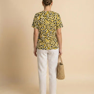 Woman in a yellow and black dotted t-shirt, white pants, holding a straw tote bag