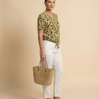 Woman wearing yellow patterned blouse, white pants, carrying straw tote bag and sandals