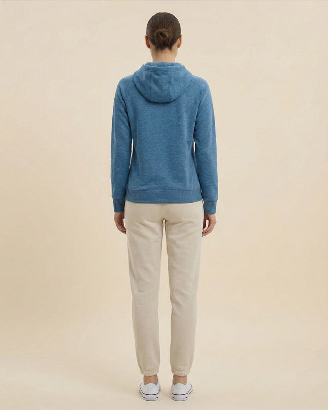 Woman in blue hoodie and beige jogger pants, standing against a plain light background