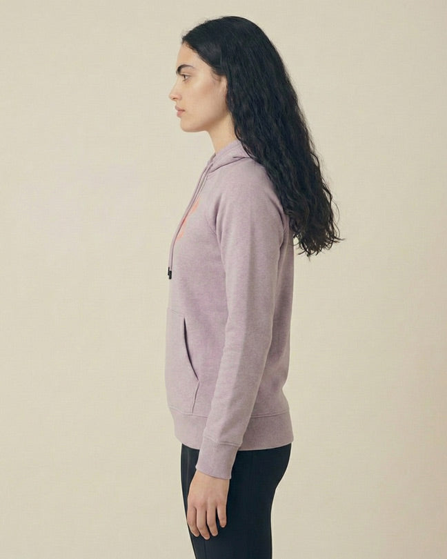 Woman in light purple hoodie and black leggings standing in profile against a neutral background