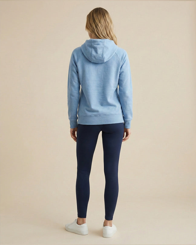 Woman wearing a light blue hoodie and navy leggings standing indoors, back view