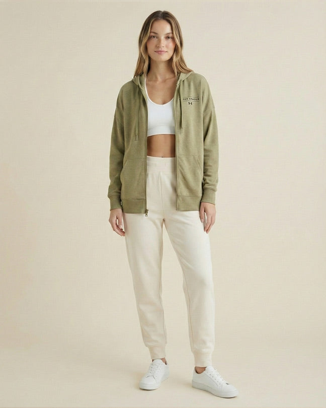 Woman wearing olive zip hoodie, white crop top, cream joggers, and white sneakers