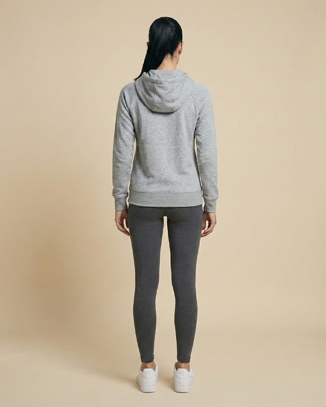 Woman in grey hoodie and dark leggings, standing back view on beige background