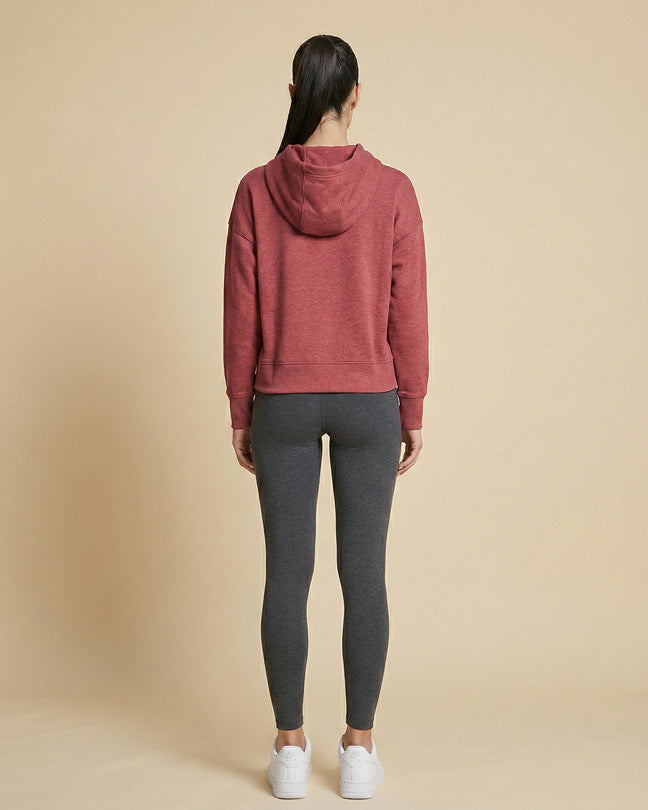Woman wearing a red hoodie, dark gray leggings, and white sneakers, facing away