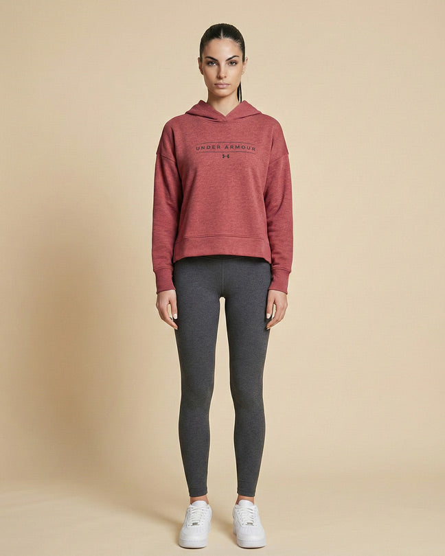 Woman in red Under Armour hoodie, gray leggings, and white sneakers standing against beige background