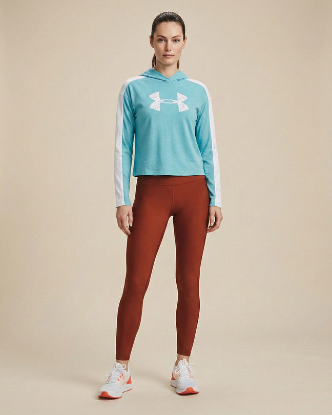 Woman in turquoise hooded athletic sweatshirt, brown leggings, and white sneakers standing indoors