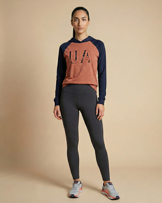 Woman in athletic wear, wearing a UA hoodie, black leggings, and running shoes, standing indoors