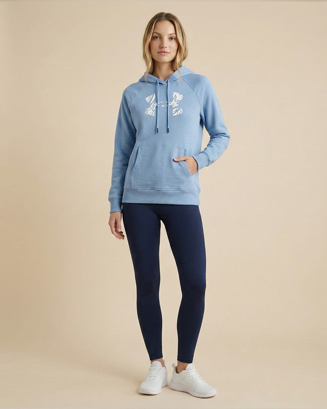 Woman in blue graphic hoodie, navy leggings, and white sneakers posing against beige background
