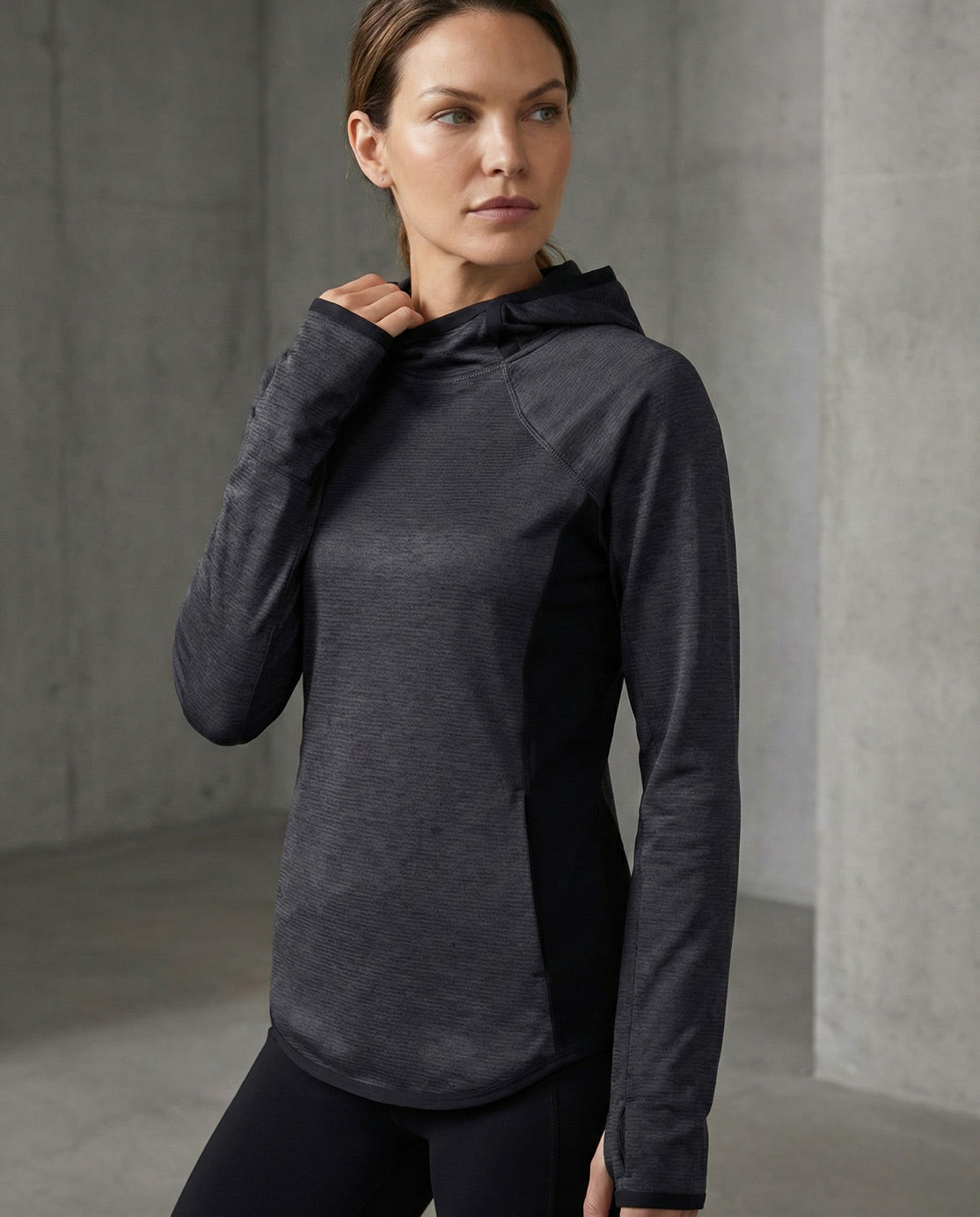 Woman wearing a dark grey athletic hoodie in a minimal concrete setting
