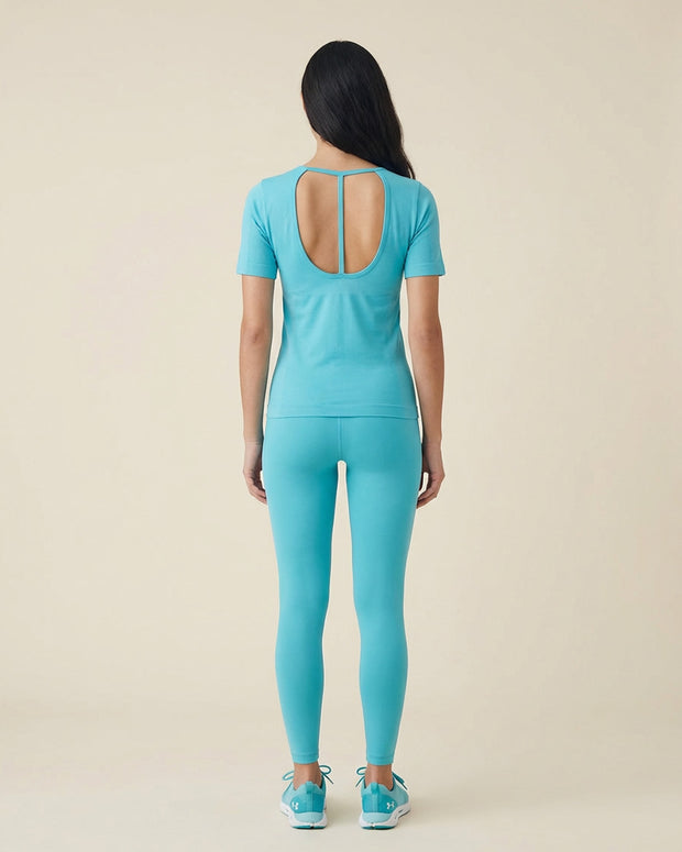 Woman wearing light blue athletic shirt with open back and matching leggings, rear view