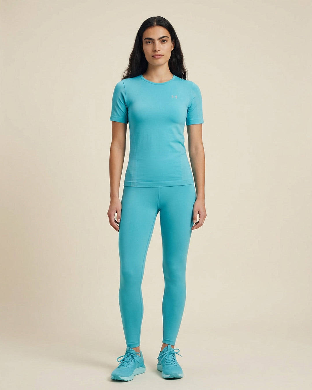 Woman wearing fitted light blue athletic shirt, matching leggings, and sneakers, standing indoors
