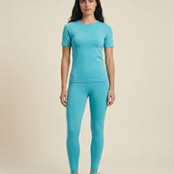 Woman wearing fitted light blue athletic shirt, matching leggings, and sneakers, standing indoors