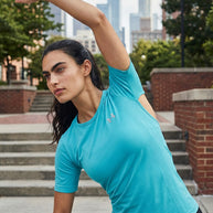 Woman stretching outdoors in a light blue athletic shirt with city buildings in background