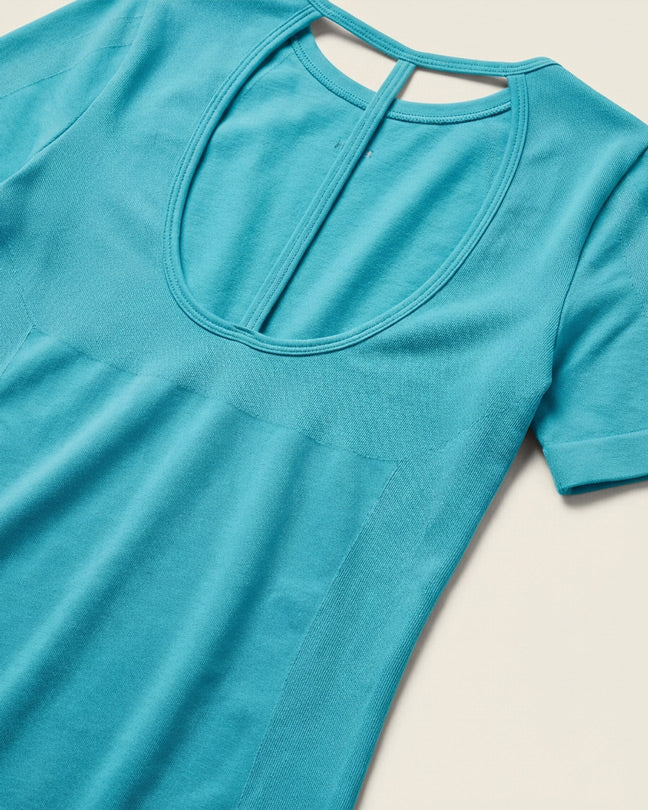 Light blue short sleeve shirt with scoop back cutout, laid flat on cream background