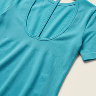 Light blue short sleeve shirt with scoop back cutout, laid flat on cream background