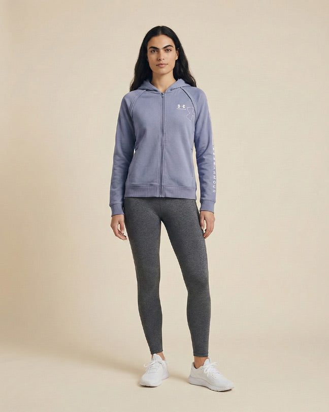 Woman wearing a light purple zip-up hoodie and gray leggings, standing on a neutral background