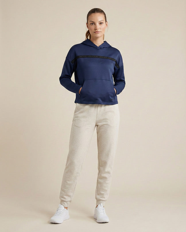 Woman in blue hoodie and beige joggers with white sneakers, posing against a neutral background