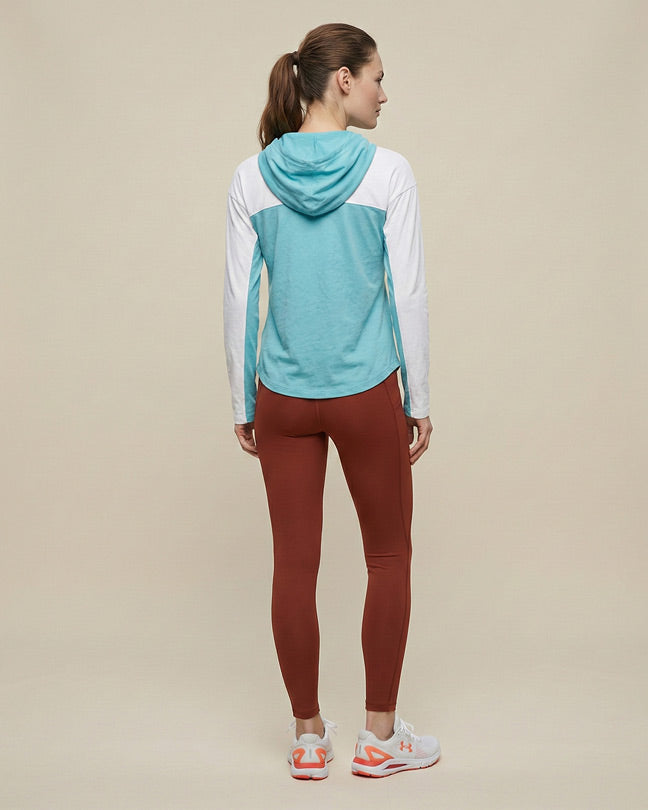 Woman in aqua and white hoodie with rust leggings and white sneakers, facing away