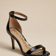 Black patent leather high heel sandal with ankle strap on beige background
