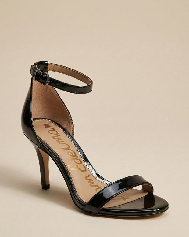 Black patent leather high heel sandal with ankle strap on beige background