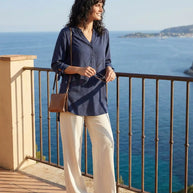 Woman in navy blouse and white pants standing on balcony overlooking ocean view