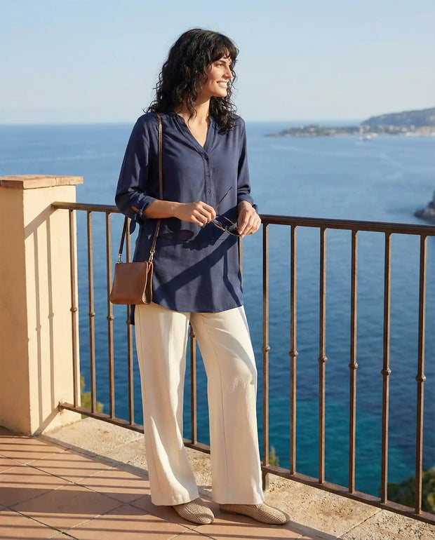 Woman in navy blouse and white pants standing on balcony overlooking ocean view