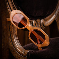 Geometric orange sunglasses with tinted lenses on a vintage wooden chair