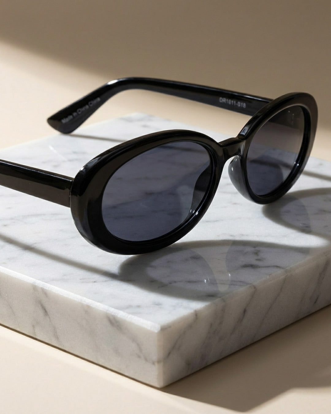 Black oval sunglasses with dark lenses on a marble slab, stylish eyewear photography