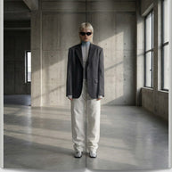 Woman in oversized blazer, turtleneck, and white pants standing in modern minimalist room