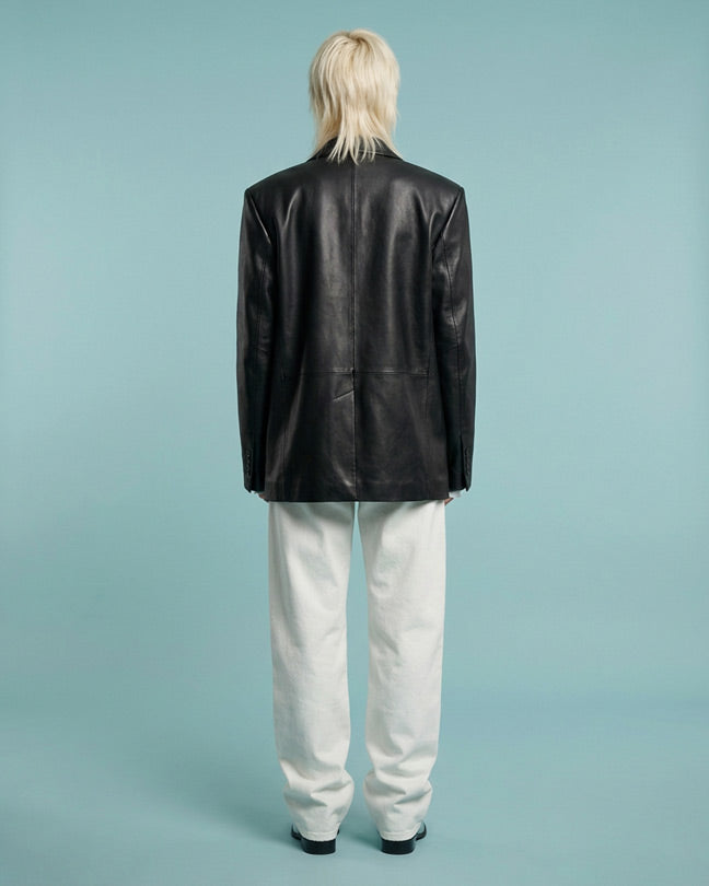 Person wearing black leather jacket and white pants, standing against light blue background
