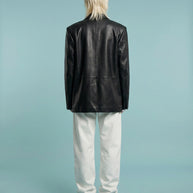 Person wearing black leather jacket and white pants, standing against light blue background