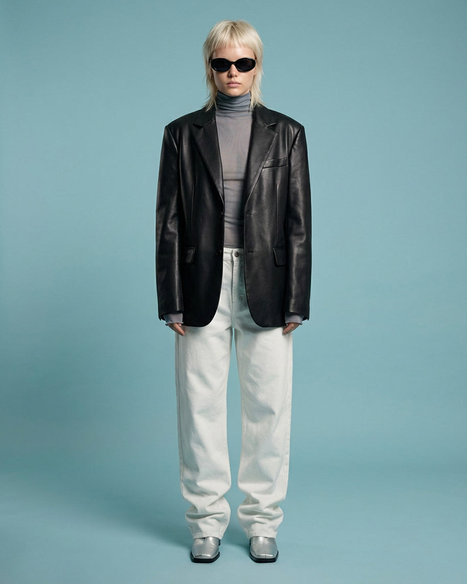 Person in a black leather blazer, gray turtleneck, white pants, and sunglasses on blue background