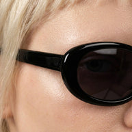 Close-up of person wearing glossy black oval sunglasses with dark lenses