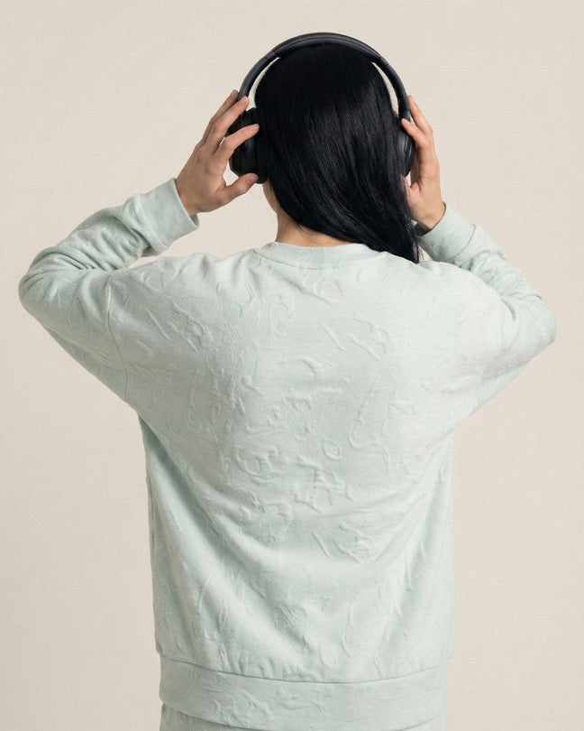 Person in light mint textured sweatshirt and headphones, seen from behind, neutral background