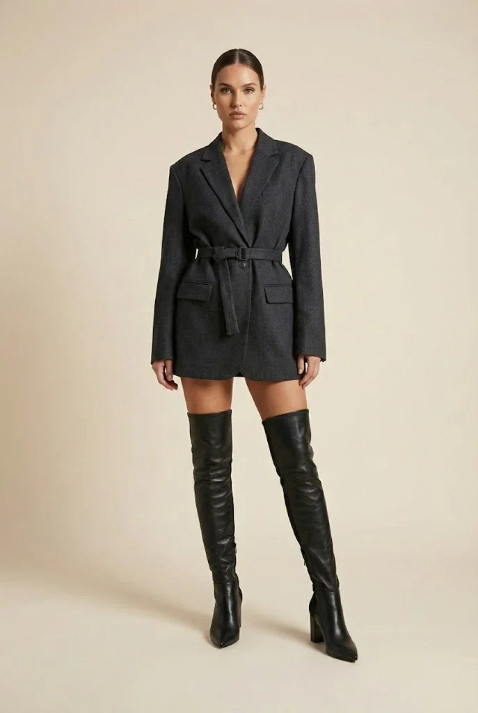 Woman wearing a belted dark blazer dress with long sleeves and black over-the-knee boots