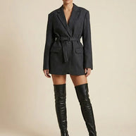 Woman wearing a belted dark blazer dress with long sleeves and black over-the-knee boots