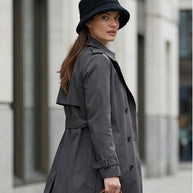 Woman in gray trench coat and black bucket hat holding brown leather briefcase outdoors