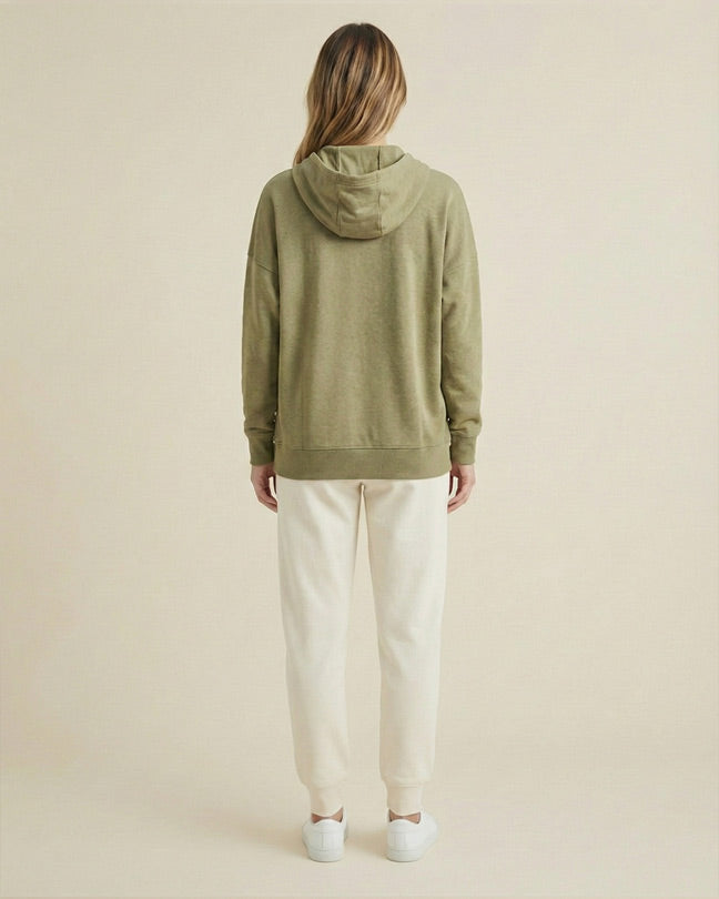 Woman in olive green hoodie and cream joggers standing with back facing, casual outfit